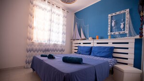 Ein Schlafzimmer mit einem Bett, einem Nachttisch, einem Fenster mit Vorhängen und einer Wand mit einem dekorativen Gegenstand.
