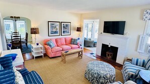 A living room with a pink sofa, blue armchairs, a fireplace, and a TV. - Classic Beach Cottage In Town (Rehoboth Beach)