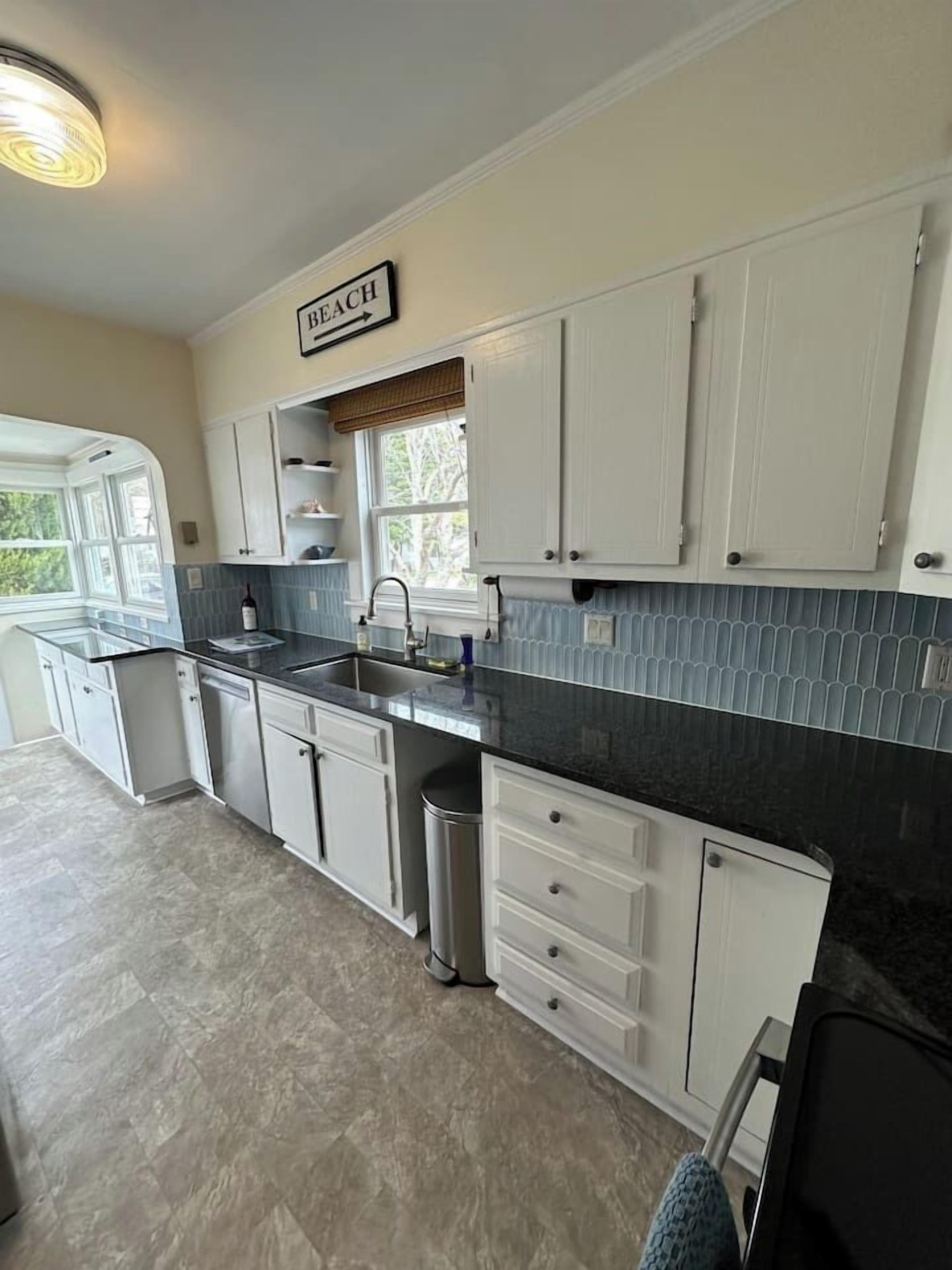 A kitchen with white cabinets, a black countertop, and a window with a view of trees.
