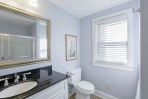A bathroom with a large mirror, a white toilet, and a window with blinds. - Classic Beach Cottage In Town (Rehoboth Beach)