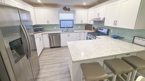 A modern kitchen with white cabinets, stainless steel appliances, a large island with bar stools, and a skylight.
