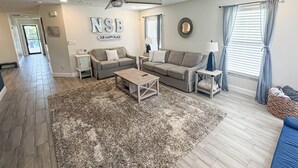 A spacious living room with a grey sofa, a coffee table, and a ceiling fan.