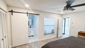 A bedroom with a bed, a ceiling fan, a sliding door, and a window with blinds.