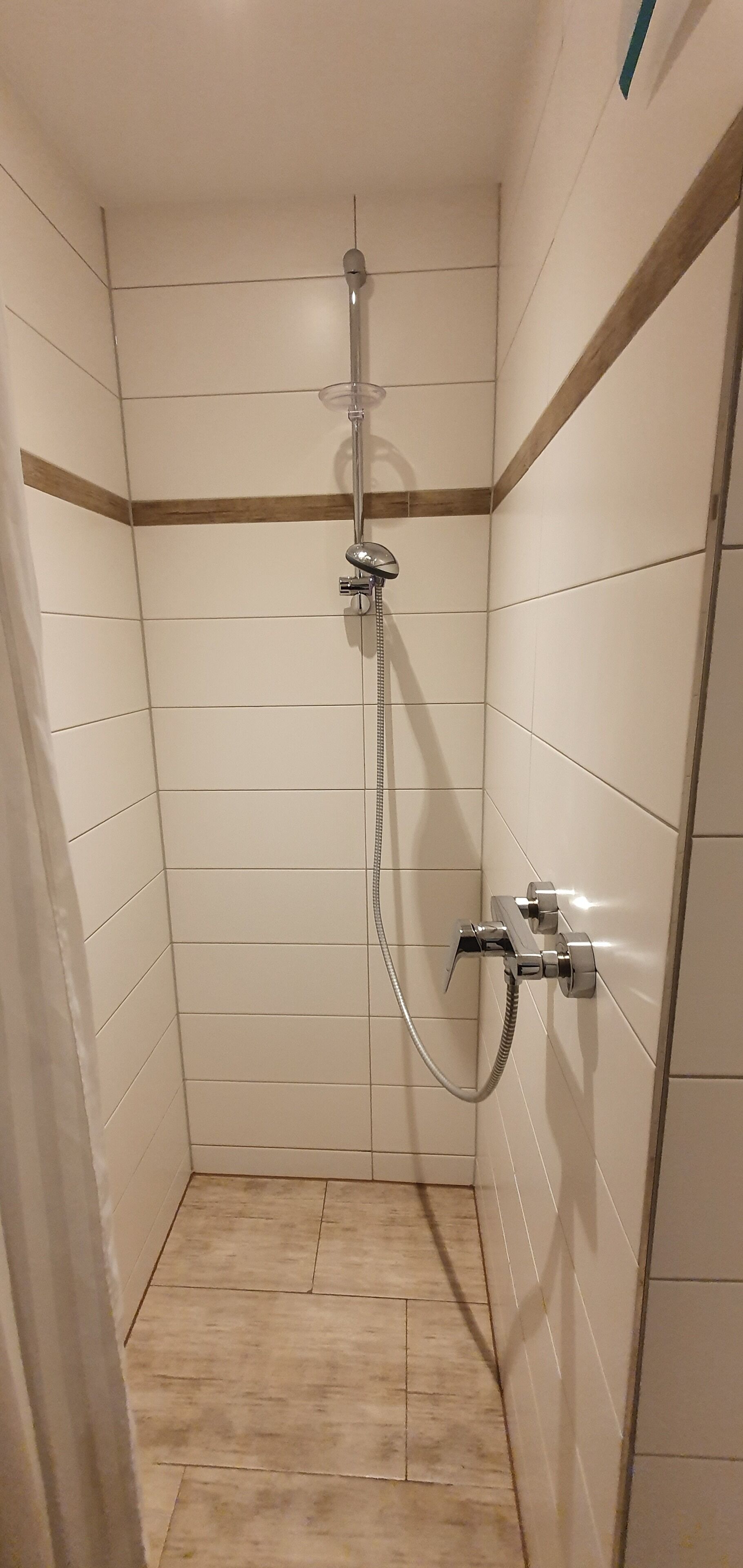 Une petite salle de douche carrelée, équipée d’un pommeau de douche et d’un flexible.