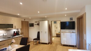 Eine kompakte Küche mit modernen Geräten, ein Essbereich mit einem Stuhl und ein an der Wand befestigter Fernseher.