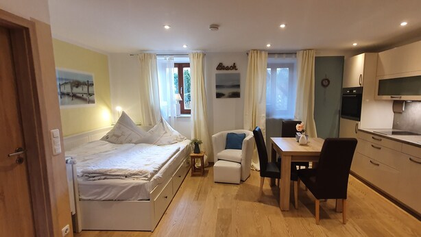Ein kleines Zimmer mit einem Bett, einem kleinen Esstisch und einer Küchenzeile.