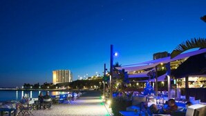 Un restaurante frente a la playa con terraza, vista al mar y un edificio al fondo.