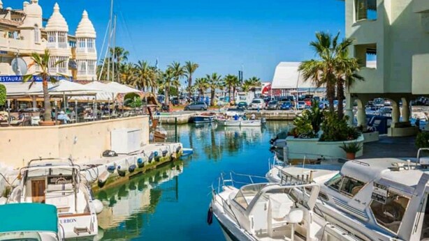 Un puerto deportivo con barcos amarrados, un restaurante y un edificio de fachada blanca.