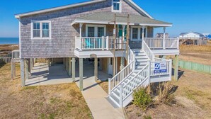 Ein zweistöckiges Strandhaus mit Balkon und Veranda, in Strandnähe gelegen.