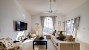 A living room with a flat-screen TV, a ceiling fan, a sofa, a coffee table, and a window with curtains. - Disney Area Superior Deluxe With Gameroom (Davenport)