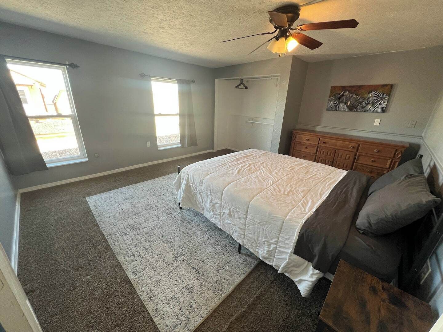 A bedroom with a bed, a ceiling fan, a dresser, and a window.