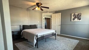 Ein Schlafzimmer mit einem Bett, einem Deckenventilator, einer Tür und einem Gemälde an der Wand.