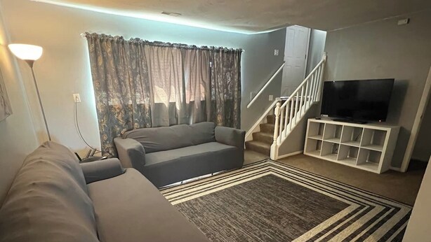 Ein Wohnzimmer mit einer Couch, einem Fernseher auf einem Schrank, einer Treppe und einem gemusterten Teppich.