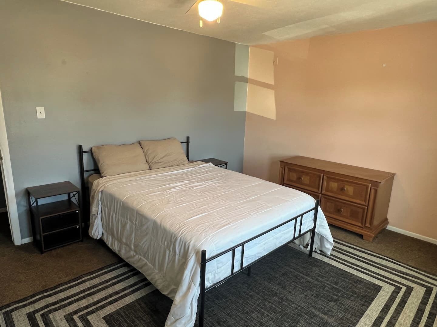 Een slaapkamer met een bed, nachtkastjes, een kaptafel en een kamerkleed met een patroon.