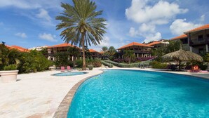 Een resort met een groot zwembad, palmbomen en gebouwen met rode daken.