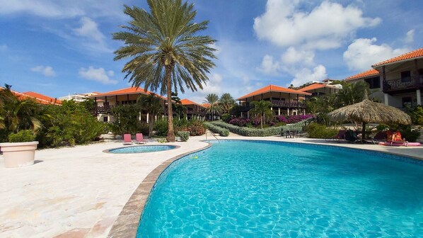 Ein Resort mit großem Pool, Palmen und Gebäuden mit roten Dächern.