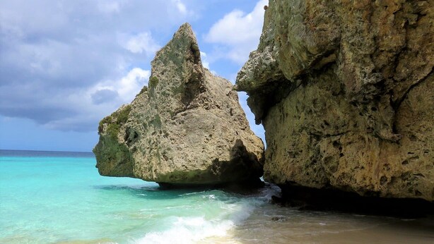 Een strand met helder turquoise water, grote rotsformaties en een zandstrand.