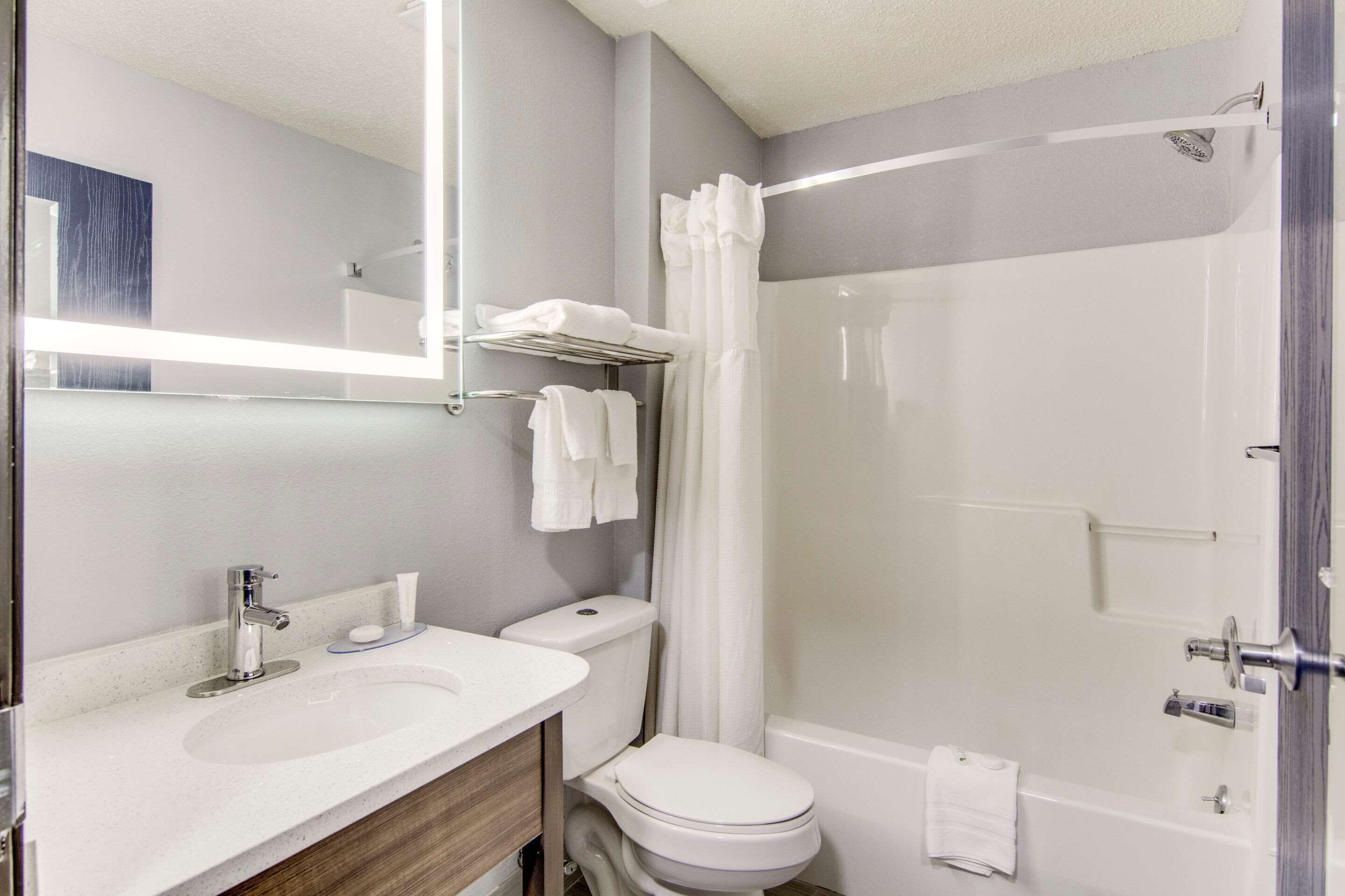 A modern bathroom with a white sink, toilet, and bathtub. There is a shower curtain, a towel rack, and a mirror above the sink.