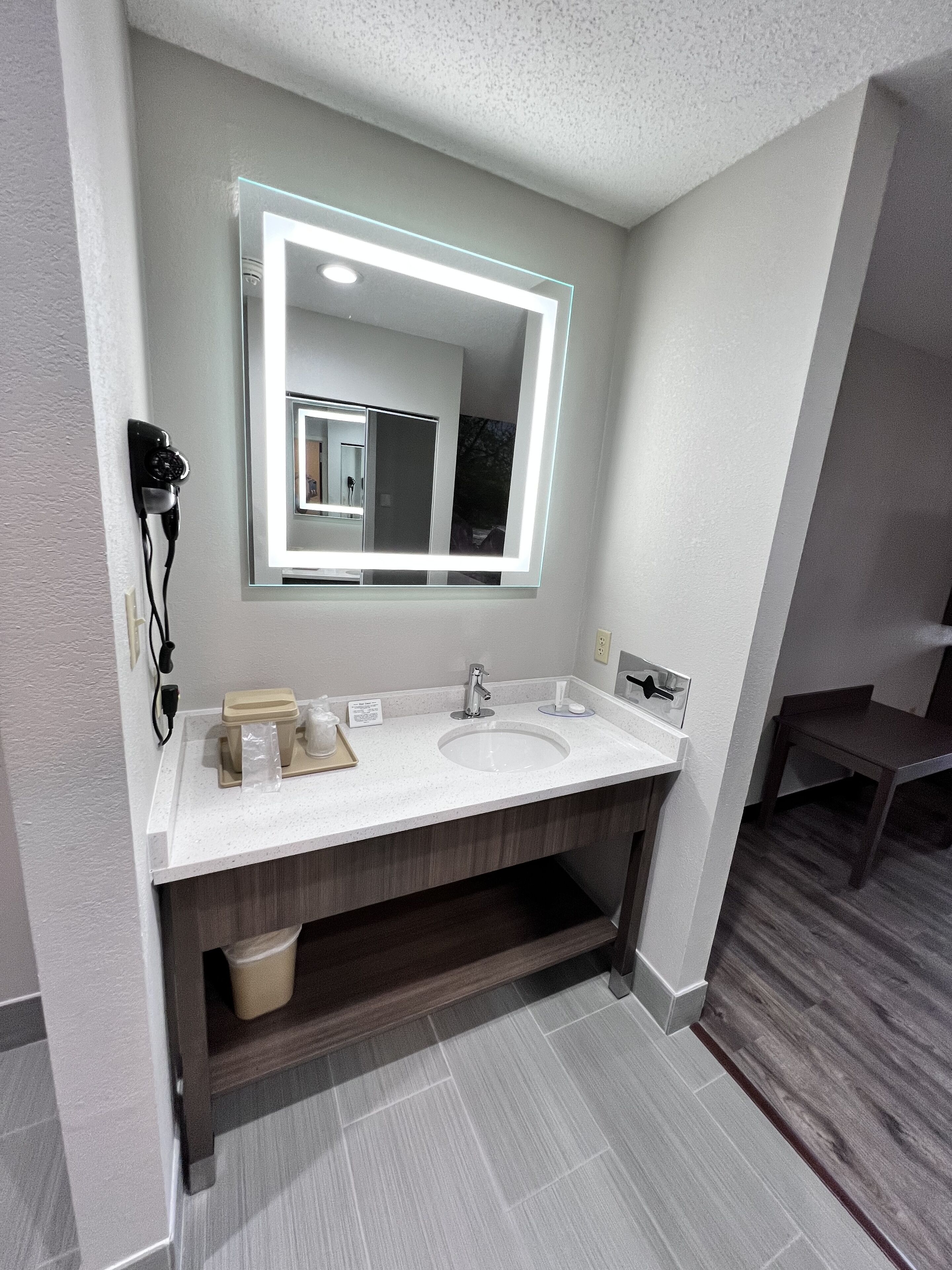 A modern bathroom with a white sink, a large mirror, and a hairdryer on the wall.