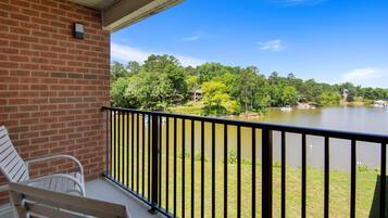 A balcony with a brick wall, a metal railing, and two white chairs.