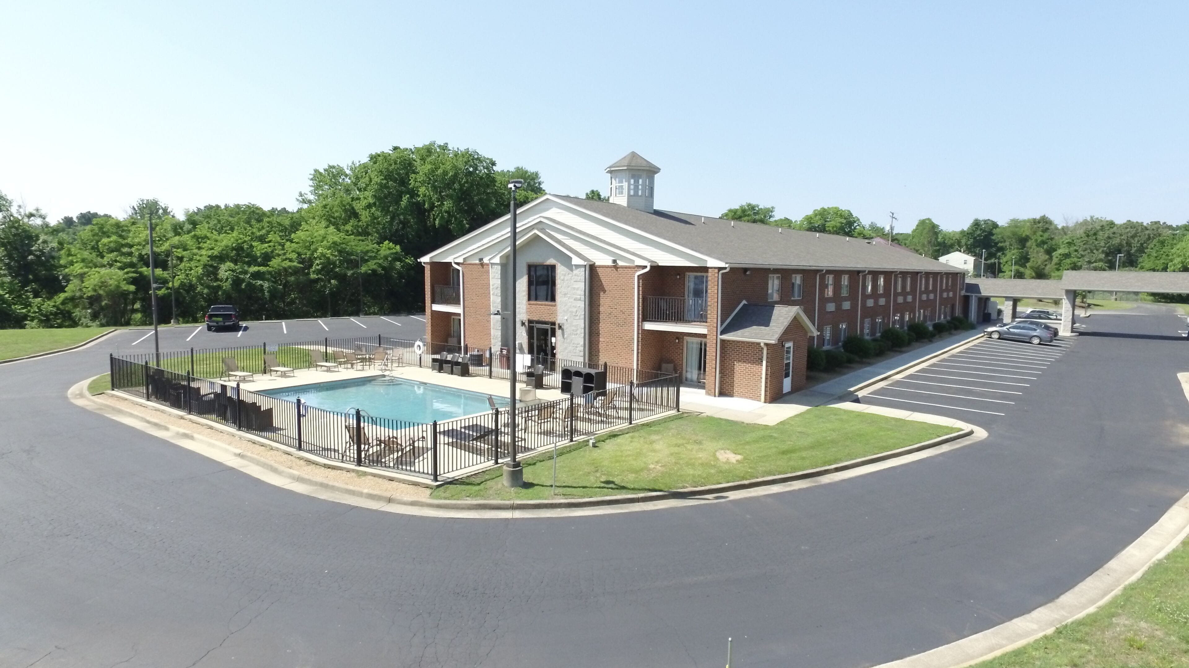 A building with a swimming pool, parking lot, and a small garden area.