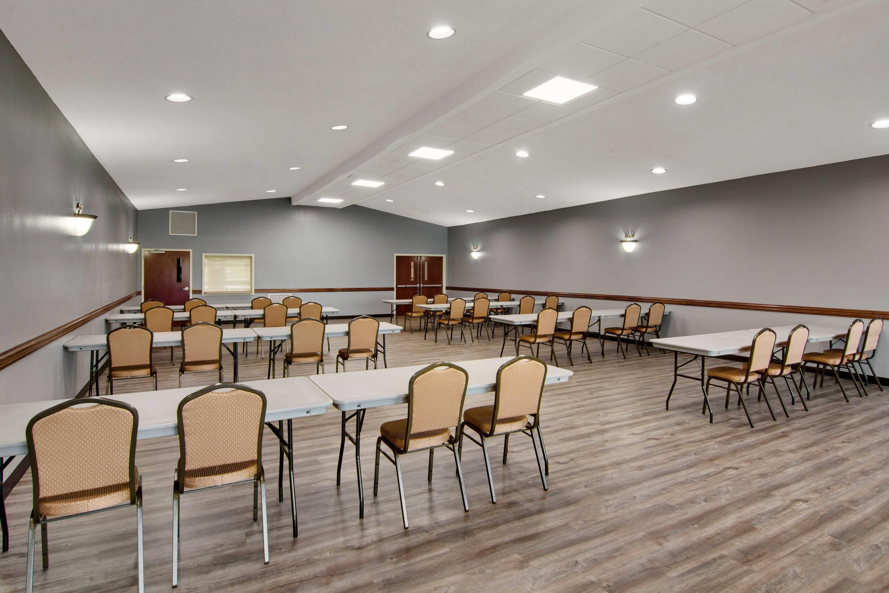 A large conference room with multiple tables and chairs, equipped with ceiling lights and a wooden floor.