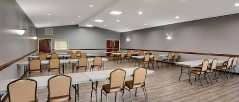 A large conference room with multiple tables and chairs, equipped with ceiling lights and a wooden floor.