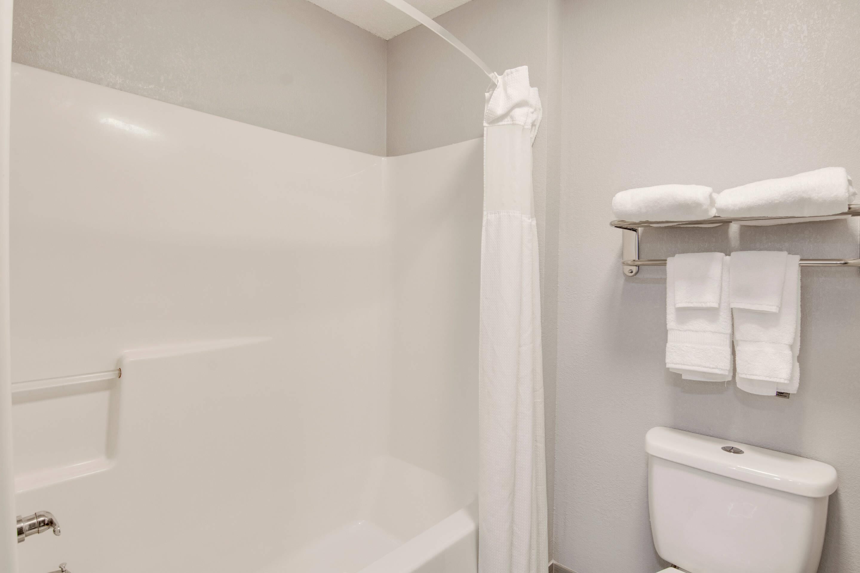 A bathroom with a bathtub, a toilet, and a towel rack with folded towels.