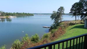 A lakeside view with a dock, grassy areas, and a bridge in the distance.