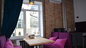 A cozy room with a brick wall, a window with a view of buildings, a table with a basket and bottles, and purple seating. - Arena and Kreshatik, best location, VIP Studio  (Київ)