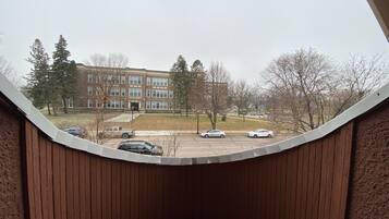 A view from a window with a curved wooden frame, overlooking a parking lot with several cars and a multi-story building with a brick facade.