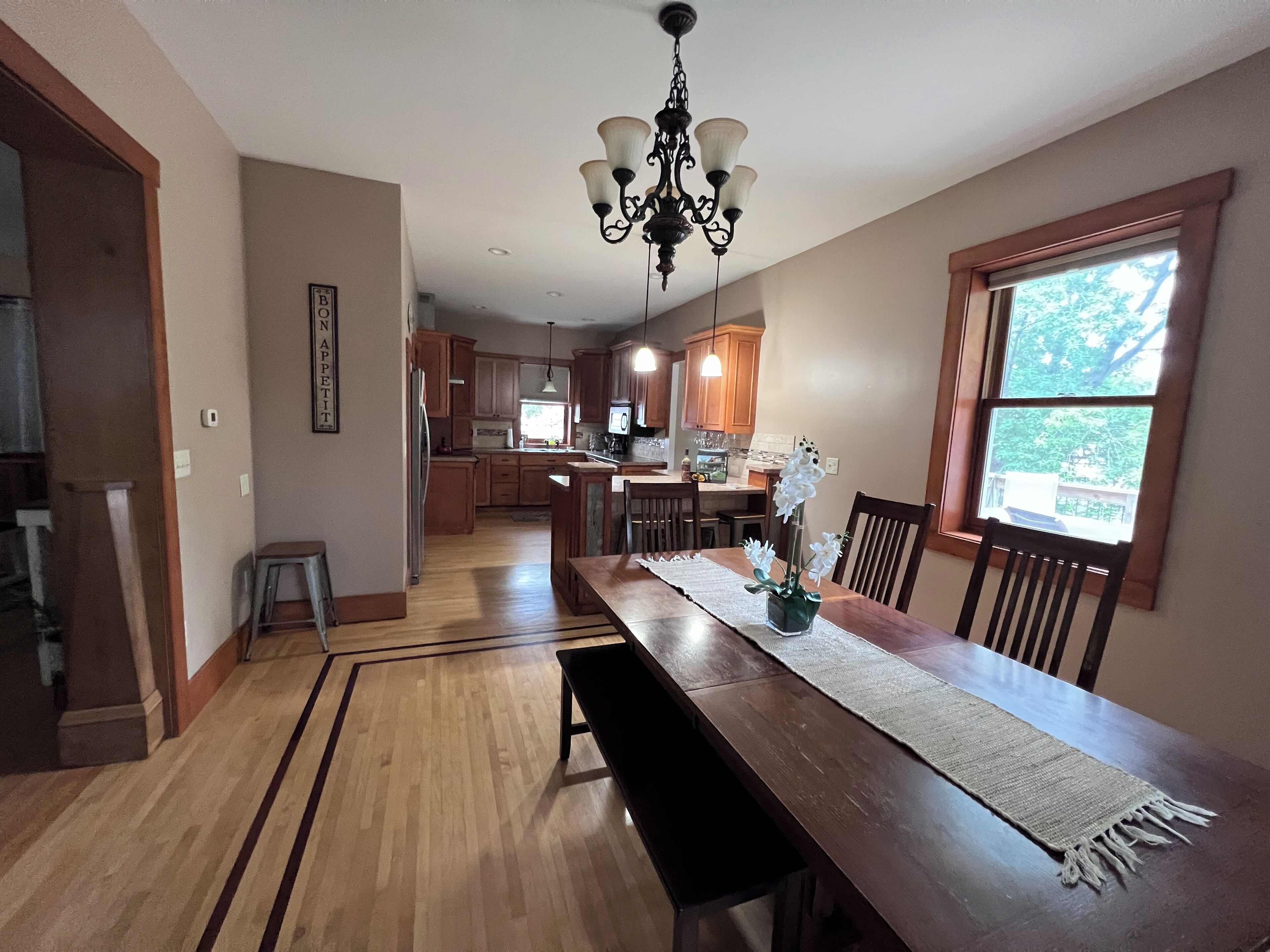 A spacious kitchen with wooden cabinets, a dining table with benches, and a chandelier.