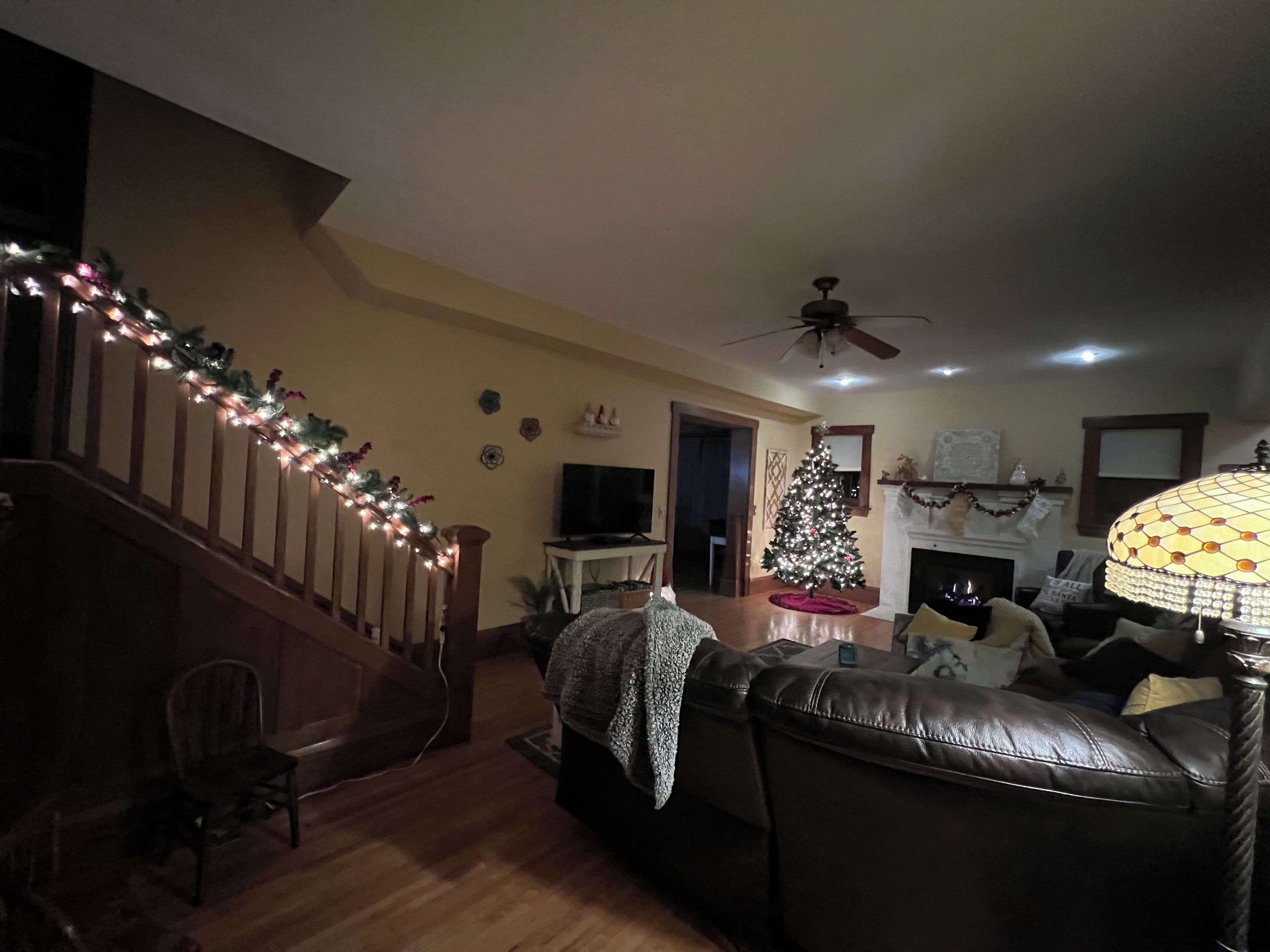 Un salon avec un escalier, un sapin de Noël, une cheminée et un ventilateur de plafond.