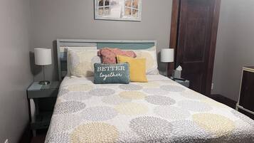 A neatly made bed with a patterned bedspread, a pillow with the text "BETTER together," and a decorative wall piece above it.