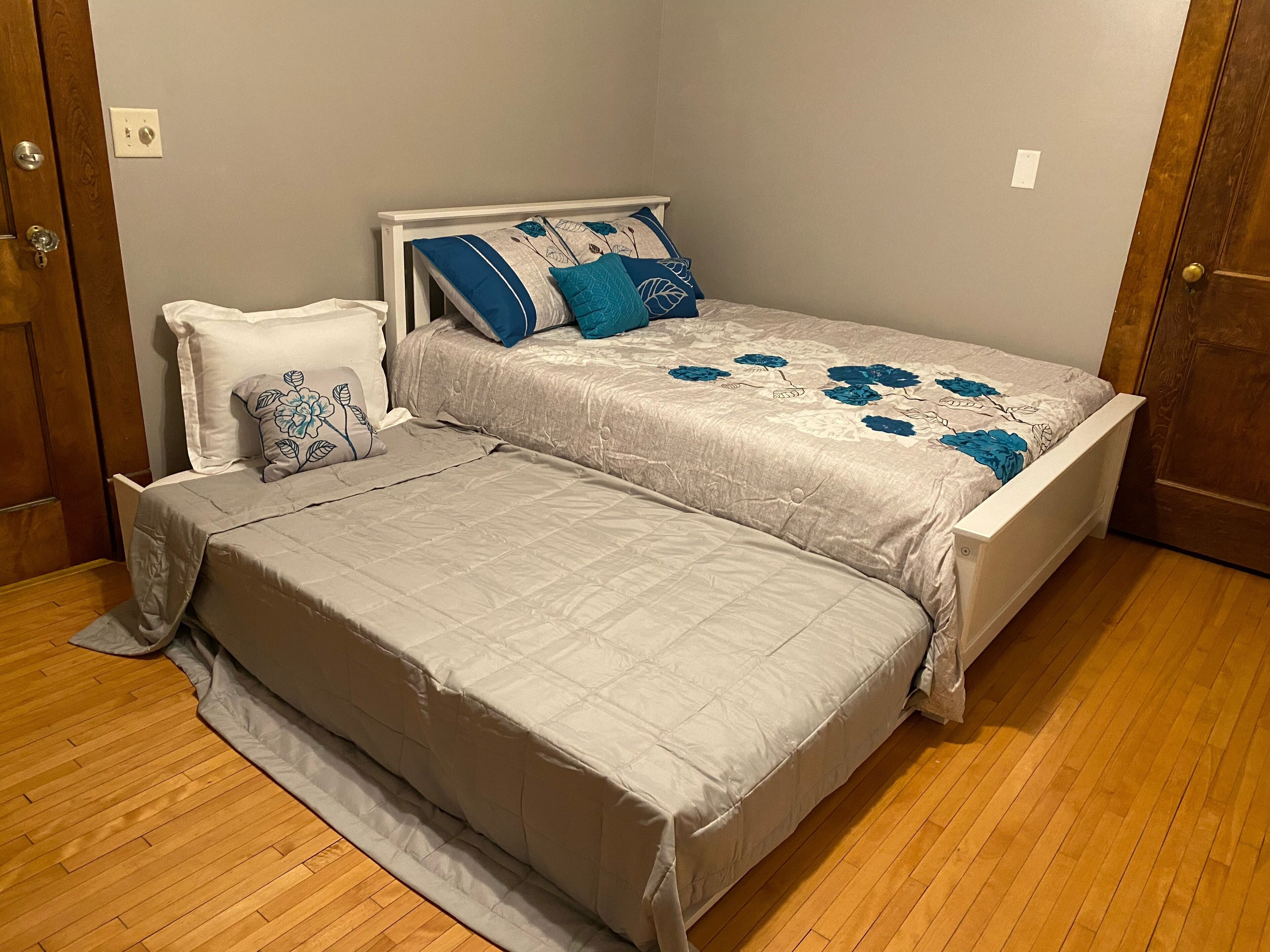 Een slaapkamer met twee bedden, een houten vloer en een grijze wand.