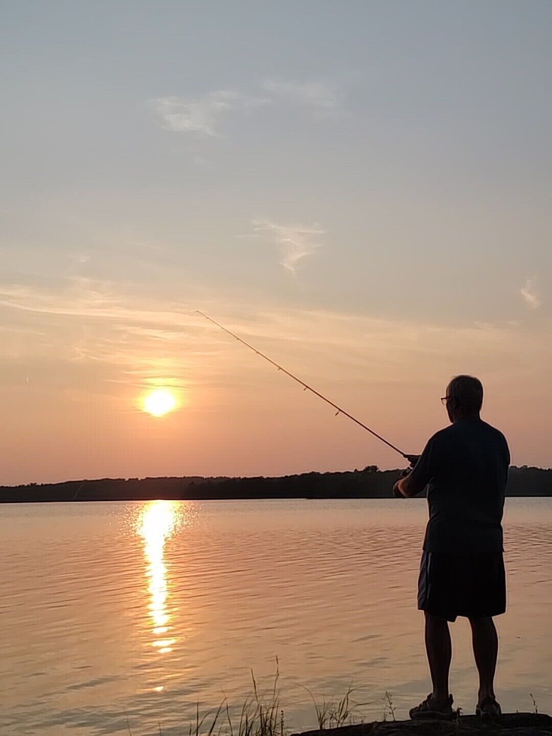 Eine Person beim Angeln im Abendlicht an einem stillen See.