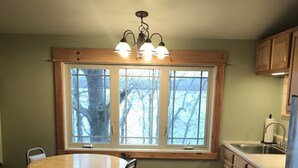 Une cuisine avec une table et des chaises en bois, une fenêtre donnant sur des arbres et des placards en bois.