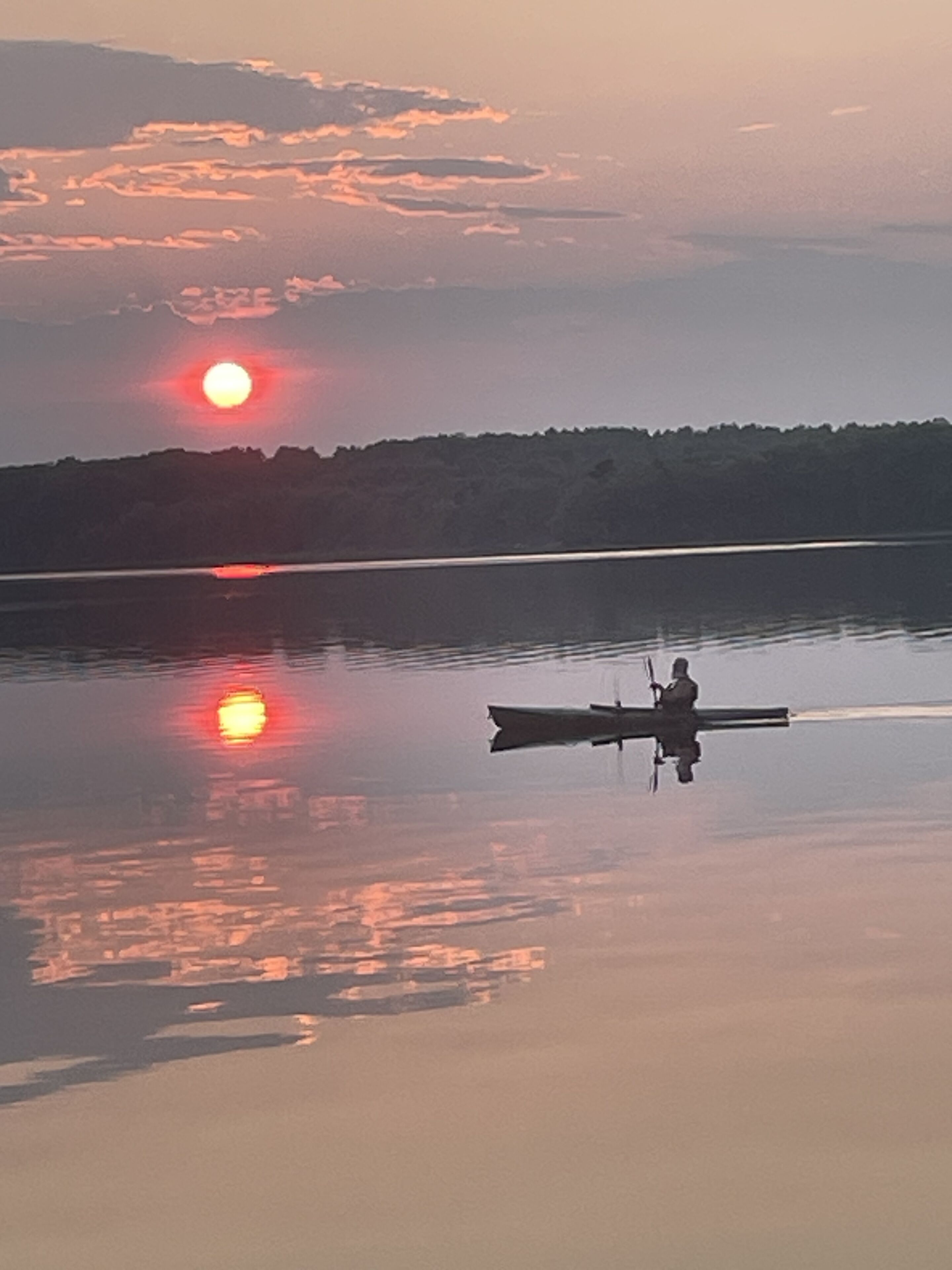 Un lago tranquilo al atardecer con un bote y una persona remando.