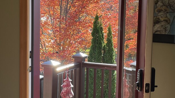 Une terrasse en bois avec une porte vitrée donnant sur un paysage d’arbres aux couleurs automnales.