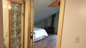 Un couloir étroit, doté d’un plancher en bois, mène à une chambre avec un lit et à une pièce de style « loft » avec une cheminée.