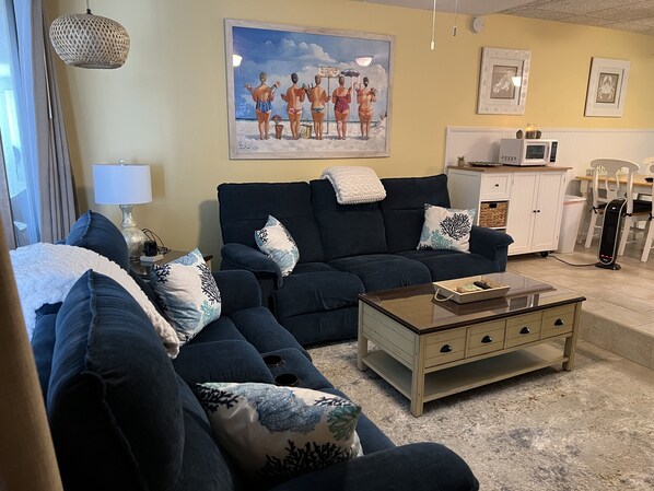 Un salon avec un canapé bleu foncé, une table basse et un tableau accroché au mur.