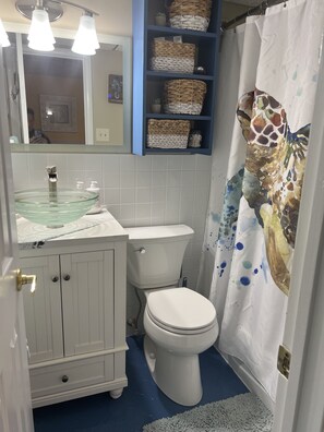 Un bagno con lavabo in vetro a forma di ciotola, vaso bianco, mensole blu con cesti e tenda da bagno a tema giraffa.
