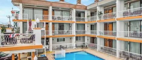 Un hotel de varios pisos con balcones, piscina y mobiliario exterior.
