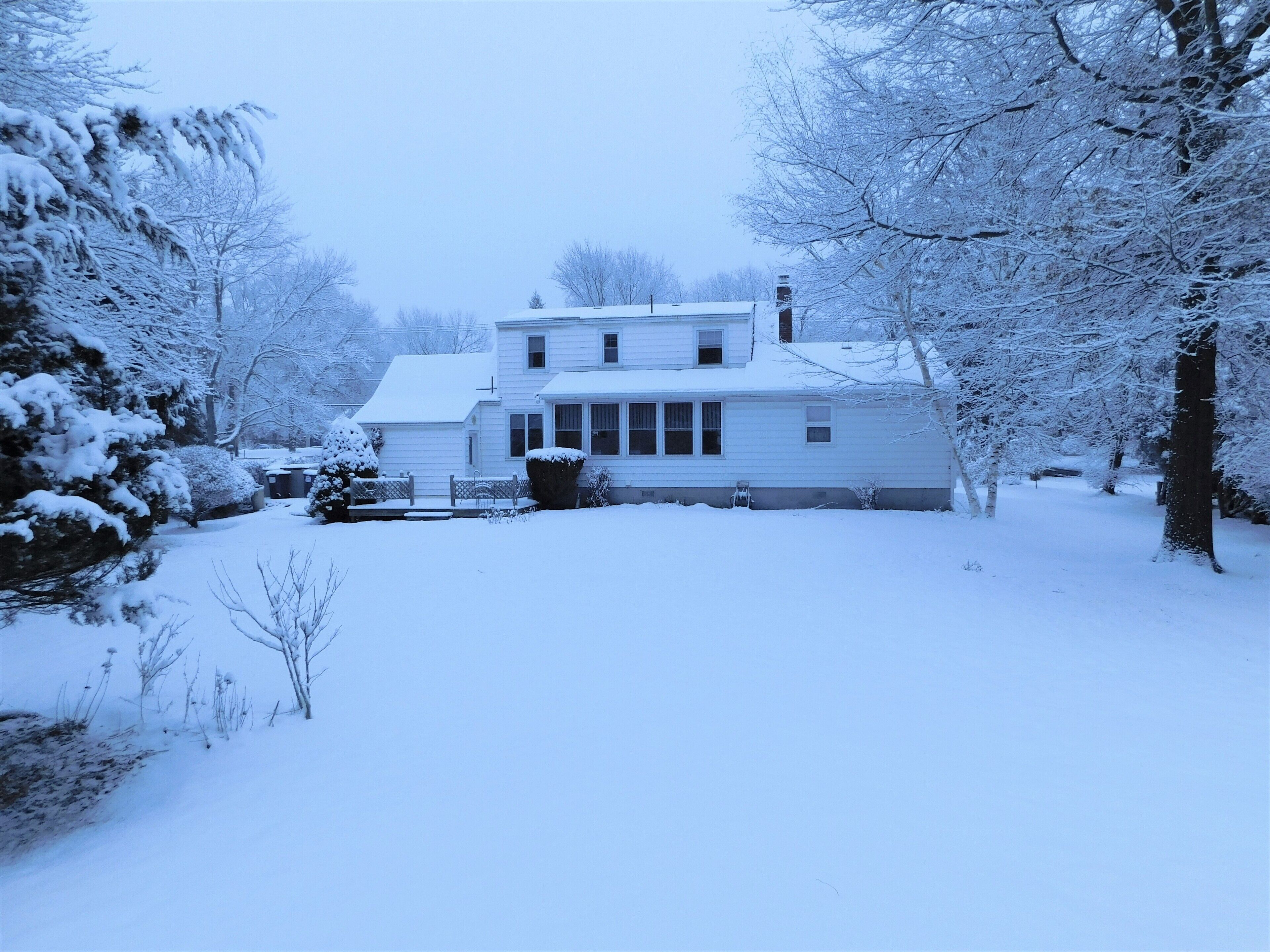 A two-story house with a snow-covered lawn and trees.
