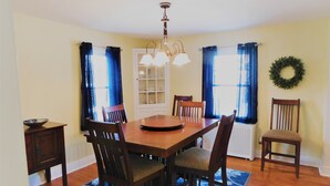 Uma sala de jantar com uma mesa de madeira, quatro cadeiras, um candelabro e uma grinalda decorativa na parede.