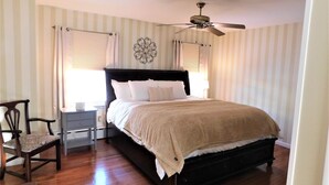 Quarto com cama, cadeira, mesa de cabeceira, ventilador de teto e papel de parede listrado.