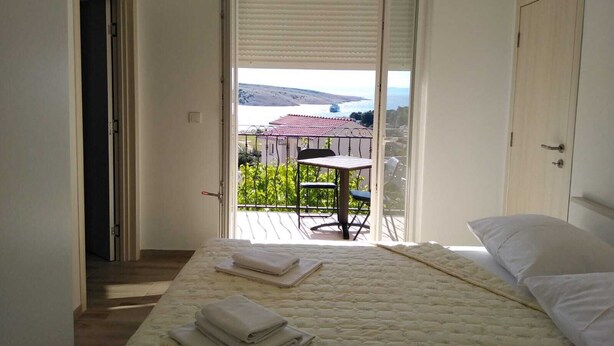 Een slaapkamer met een bed, een balkon met een tafel en stoelen, en uitzicht op een gebouw en heuvels.