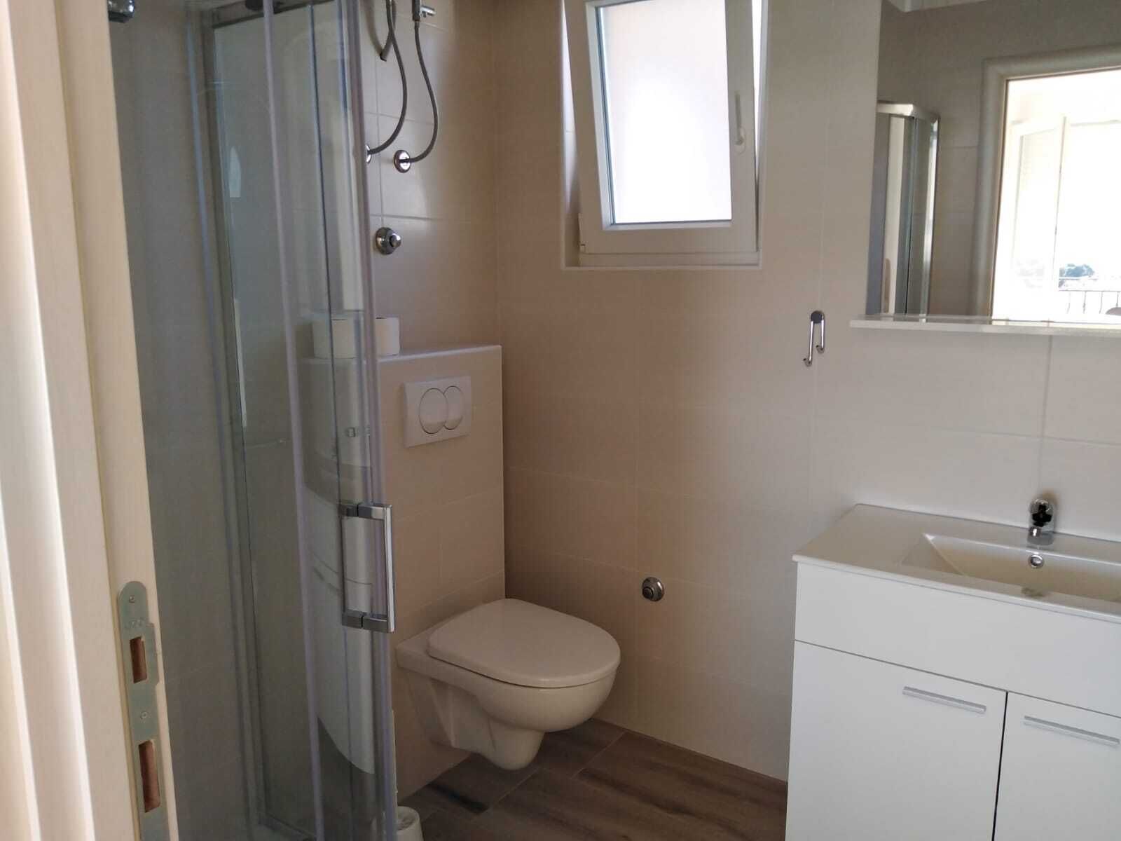 Une salle de bain avec une douche à parois de verre, des toilettes, une petite fenêtre et un lavabo avec un miroir au-dessus.