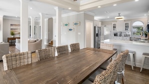 A spacious dining area with a wooden table and wicker chairs, a kitchen with white cabinets, and a ceiling fan. - Destiny West, Huge Pool/Spa, Game Room, Gulf Views, Theater, Golf Cart Rental (Destin)