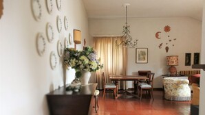 Un coin repas avec une table et des chaises en bois, un lustre et un arrangement floral posé sur une table d’appoint.